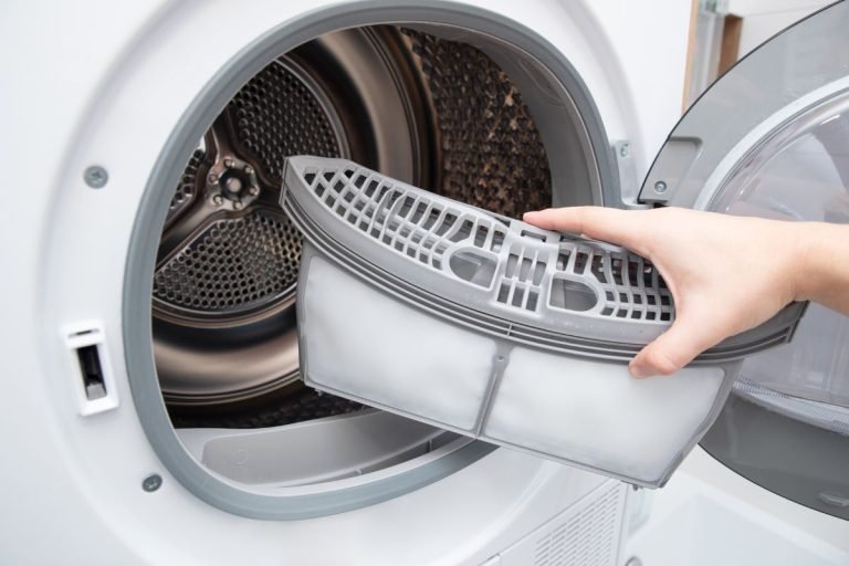 An individual is loading a basket of clothes into a washing machine for a wash cycle.