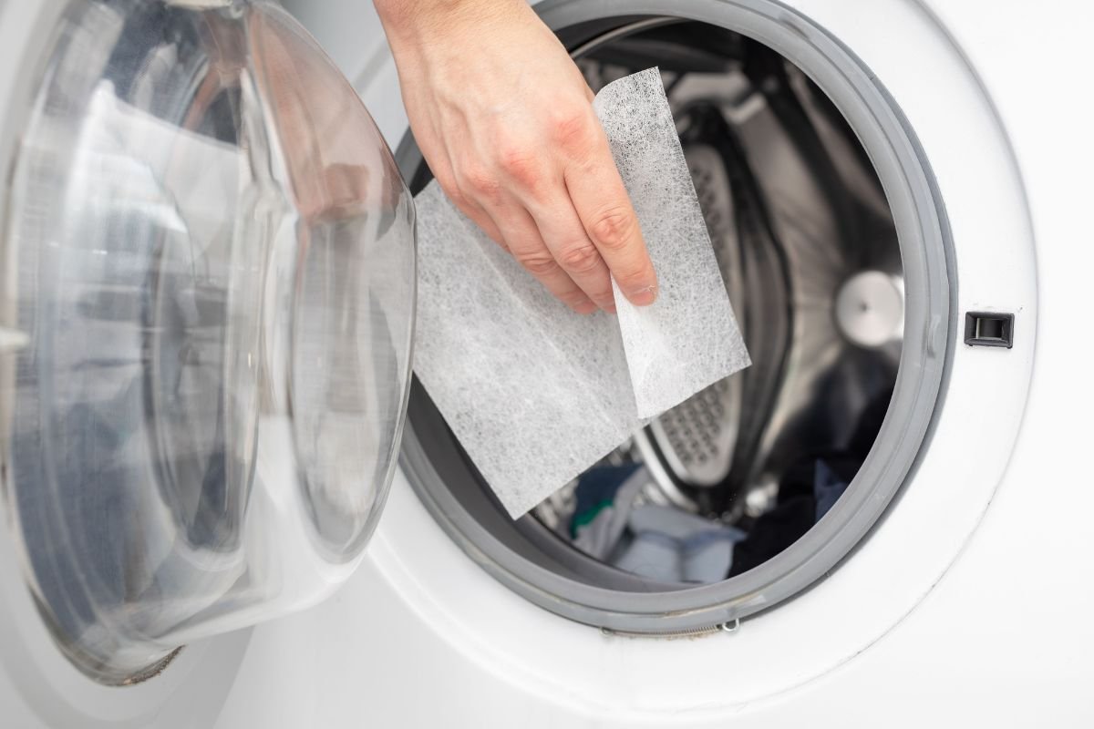 A person inserts a piece of paper into a washing machine, demonstrating an unusual action in a laundry setting.
