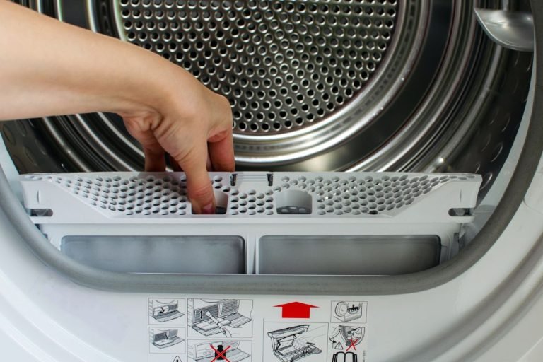 An individual inserts a small plastic item into a washing machine, readying it for washing clothes.